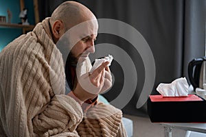 Sick man suffering from running stuffy nose and sore throat. Upset ill guy blowing her nose using paper napkin tissue