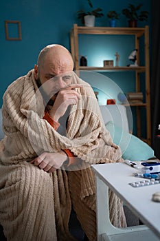 A sick man suffering from a runny nose sitting on the sofa at home holds his nose with his hand. Cold and runny nose