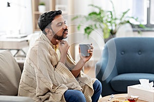 Sick man with tea touching his sore throat at home