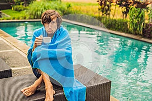 Sick man traveler. The man caught a cold on vacation, sits sad at the pool drinking tea and blows his nose into a napkin