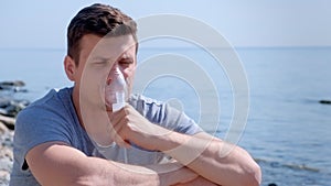 Sick man uses nebulizer inhaler mask to treatment of fibrosis asthma on seaside.