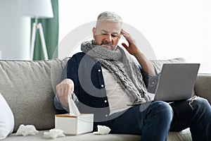 Sick mature man with laptop websurfing, home interior