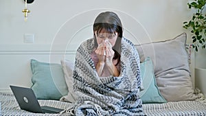 Sick mature woman with blanket, sneezing coughing blowing nose in napkin