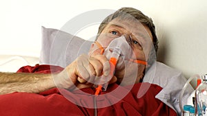 Sick middle-aged man is breathing through oxygen mask while lying in bed.