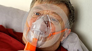 Sick middle-aged man is breathing through oxygen mask while lying in bed.