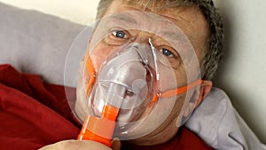 Sick middle-aged man heavy breathing through oxygen mask while lying in bed.