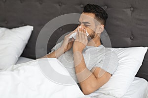 Sick Middle Eastern Man Blowing Nose In Paper Tissue In Bed