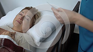 Sick-nurse covering sleeping elderly patient with blanket, taking family photo