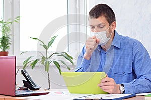 Sick office worker in medical mask sits at desk