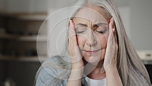 Sick old mature caucasian woman worried tired upset retiree grey-haired lady holding head massaging temples unbearable