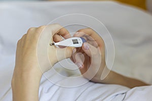 A sick person is lying in bed with a thermometer in his hands