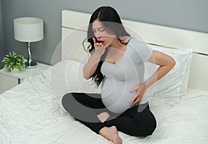 Sick pregnant woman feeling unwell and coughing on bed