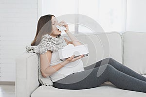 Sick pregnant woman sitting at home on the couch. She flies herself into a paper napkin.