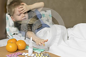 A sick sad child with a temperature and a headache lies in bed next to medication. Flu colds disease virus