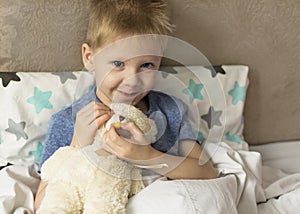 A sick sad child with a temperature and a headache lies in bed with a toy teddy bear. Flu colds disease virus