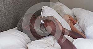Sick senior african american man couching while lying on the bed at home