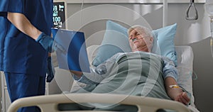 Sick senior man lying in hospital bed and signing informed consent