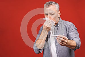 Sick senior man with thermometer, blowing his nose with tissue