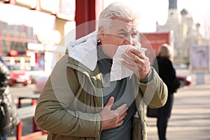 Sick senior man with tissue on city street. Influenza virus