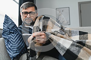 Sick senior man using thermometer checking his temperature suffering from seasonal flu or cold.