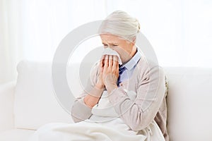 Sick senior woman blowing nose to paper napkin