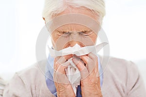 Sick senior woman blowing nose to paper napkin