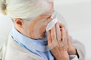 Sick senior woman blowing nose to paper napkin