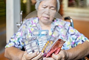 Sick senior woman holding medicine pills  in wheelchair,sad female elderly showing a lot of drugs,medication to treatment her