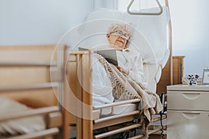 Sick senior woman lies in a hospital bed and reads a book