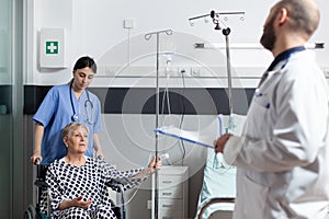 Sick senior woman sitting in wheel chair with iv drip bag attached on arm