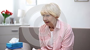 Sick senior woman sneezing in tissue at home, flu virus disease, infection