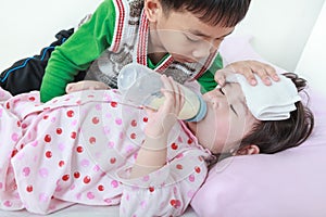 Sick sister lying and suck up milk on the bed, kindly brother keep vigil over a sick of closely.