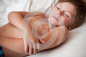 Sick small boy lying with a thermometer in the armpit
