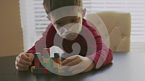 Sick small boy in a red sweater with the white respirator mask on his face is playing with the colorful wooden blocks on