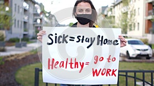 Sick - stay home healthy - go to work. Close portrait of a girl in a black protective mask with a poster. Solitary