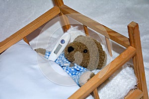 Sick teddy bear with clinical thermometer in bed