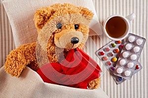 Sick teddy bear lying in bed with hot water bottle