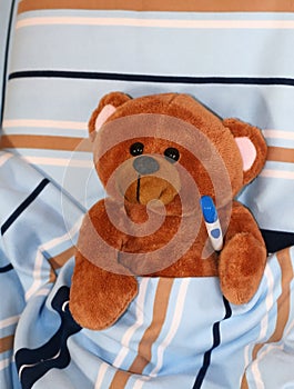 sick teddy bear with thermometer in bed