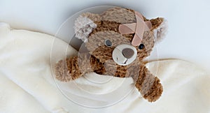 Sick teddy bear toy with patch on head lying in bed