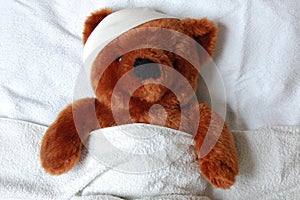 Sick teddy with injury in bed