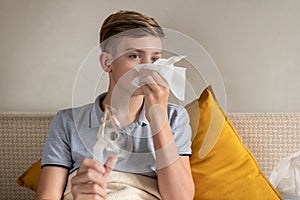 Sick teen boy with an inhaler. Unhealthy child doing inhalation at home, she use nebulizer and inhaler for the treatment