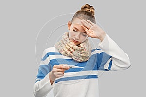 Sick teenage girl in scarf measuring temperature