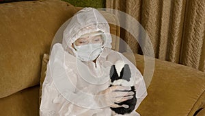 Sick teenager girl in protective costume playing with hamster on home sofa while quarantine. Diseased girl infected