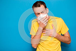 Sick tired man wearing medical mask and coughs isolated on blue background. Coronavirus, Covid-19, illness person, sore throat