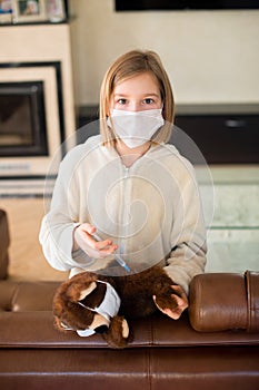 Sick toddler girl in medicine mask making vaccination her teddy bear with syringe