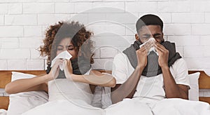 Sick african-american couple blowing noses in bed
