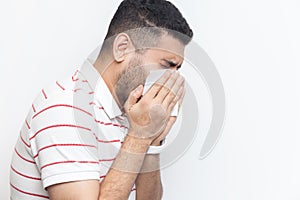 Sick unhealthy bearded man standing having runny nose, using napkin, having flu symptoms.