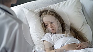 Sick weak girl lying in bed in hospital, doctor examining patient, healthcare