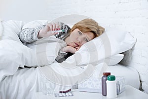 sick woman in bed checking temperature with thermometer feeling feverish having cold winter flu virus photo
