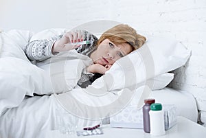 sick woman in bed checking temperature with thermometer feverish weak suffering cold winter flu virus photo
